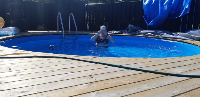 Person med dykmask i en nybyggd hemmagjord rund pool med träaltan och blått vatten under soligt väder.