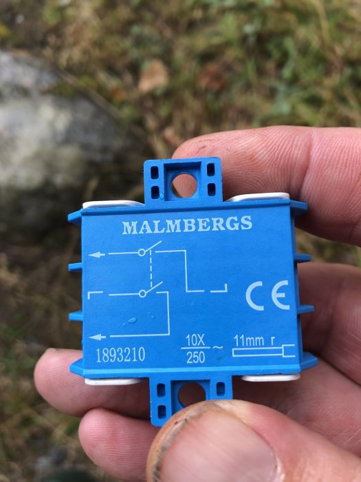 Närbild på en hand som håller en blå tvåpolig strömbrytare från Malmbergs med schema tryckt på sidan.