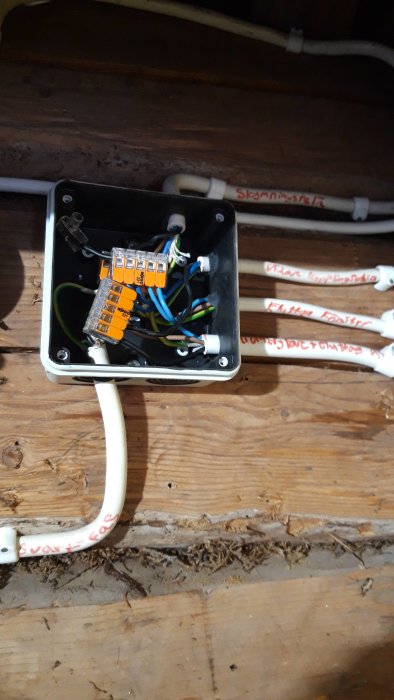 En öppen eldosa med sammankopplade kablar och märkta rör längs en trävägg, vilket visar ett slutfört elektriskt projekt.