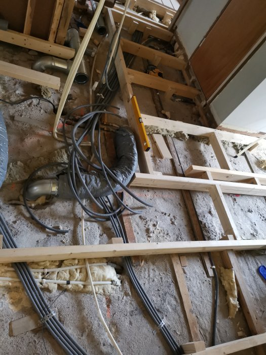 Delvis completes golvreglar och flexslangar utlagda längs ett golv i en pågående byggrenovering.