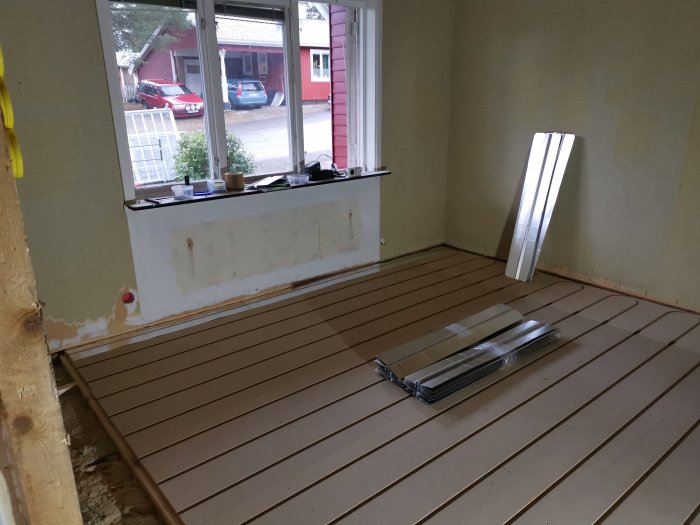 Renoveringsprojekt med nytt golv under installation i ett rum med synlig väggisolering och fönster som vetter mot en gata.