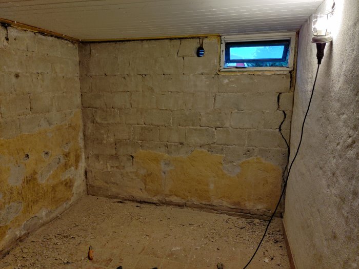 Hörn av ett rum under renovering med delvis bortskrapad gul färg på betongväggar och synliga reparationsarbeten.