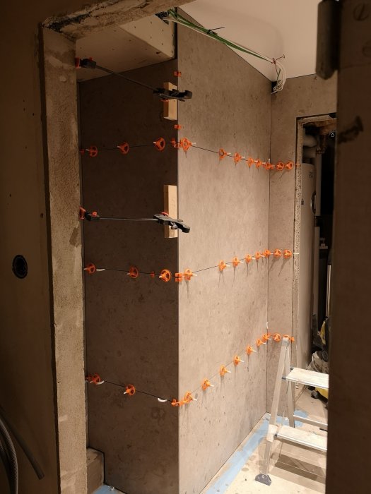 En vägg under renovering med nyinstallerade kakelplattor och orangea distansklämmor.