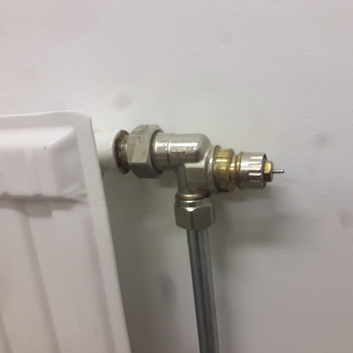 Närbild av ett element i källare utan termostat, visande kopplingar och luftskruv.