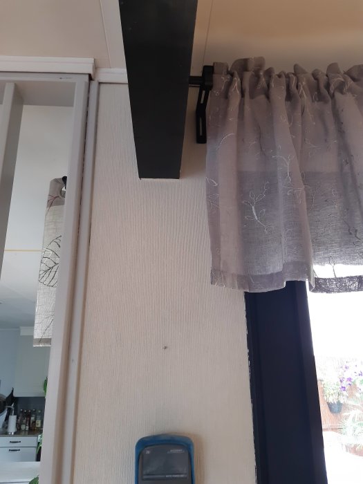 Ett gardinfäste monterat på väggen ovanför ett fönster med en hängande gardin; frustration indikeras av texten.