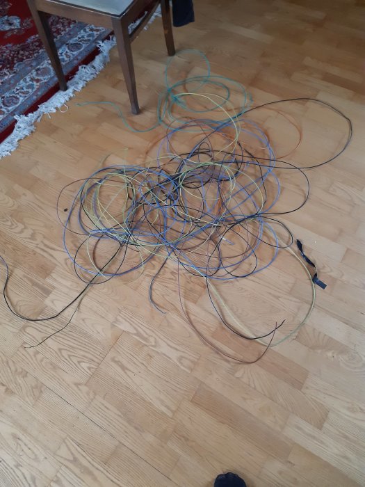 En röra av kablar i olika färger och storlekar på ett trägolv.