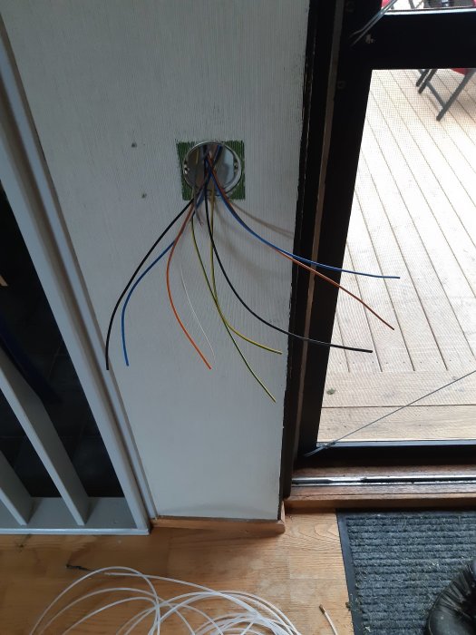 Olabeled elektriska kablar sticker ut från en öppen kontakt i en vägg vid en dörröppning.