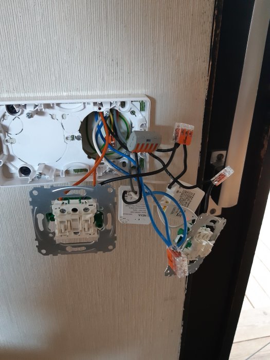 Öppen elinstallation med oskyddade eluttag och lösa kablar intill en dörrkarm.