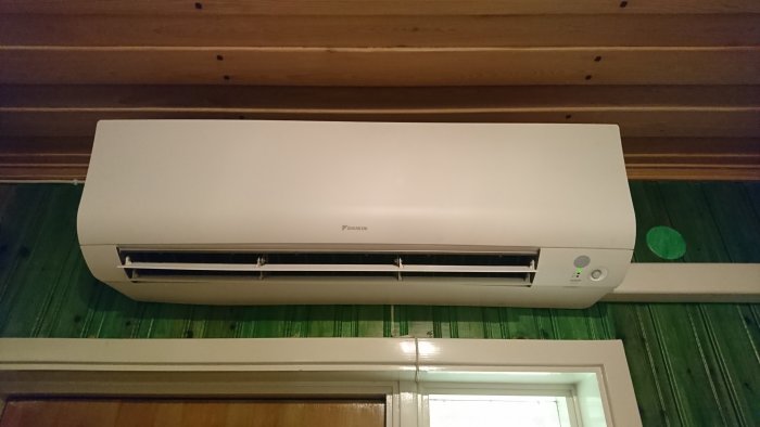 Daikin Ftxtm40 innedel luftkonditionering monterad över dörr, grön gardin i bakgrunden.