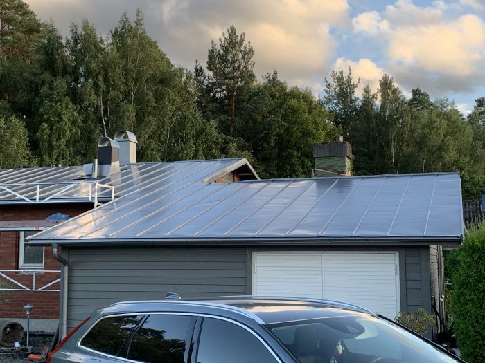 Nytt antracit metallic aluminiumtak på hus med synliga skenor och ojämnheter mot skymningen.