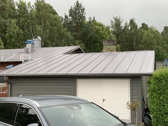 Plåttak i antracit metallic på ett hus, synliga vågor i plåten, omgivet av träd.