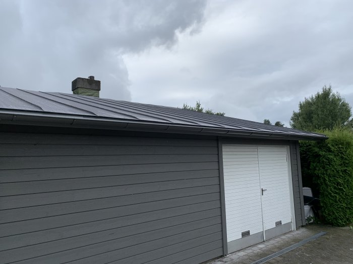 Aluminiumtak i antracit metallic med synliga vågor på ytan på ett garage, molnig himmel i bakgrunden.