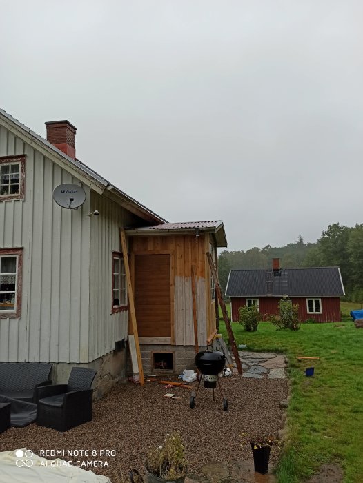 Oisolerad utbyggnad på hus med synliga reglar och takspån under ett plåttak på en mulen dag.