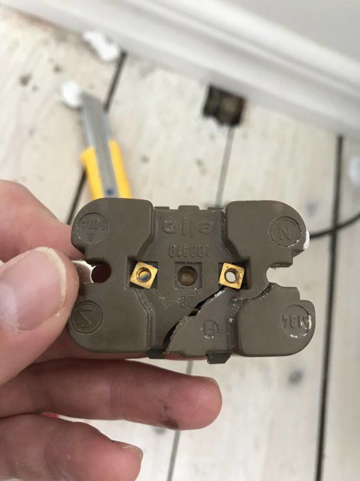 Hand håller ett utanpåliggande vägguttag med märkning för N och L över skruvanslutningar.