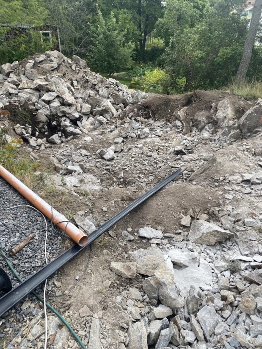 Markarbete med sprängsten och grushög vid byggplats för pool och stenmurar.