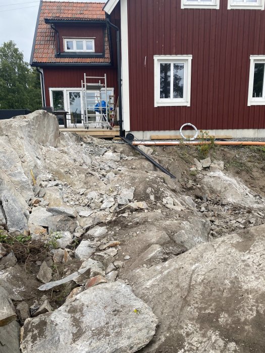 Sprängningsarbete vid ett rött hus där en berggrund har delvis röjts för att bygga en pool.