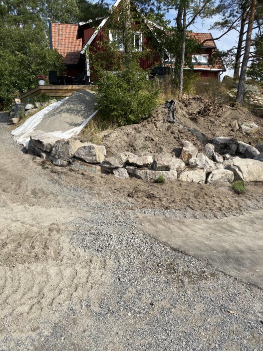 Nybyggd stenmur av sprängsten med byggplats för pool och röd stuga i bakgrunden.