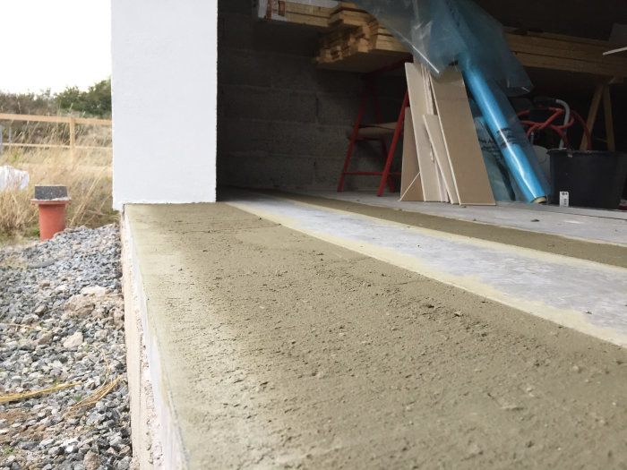 Bild på nyspacklat golv med grov sand som ger en ojämn yta nära en byggnad.