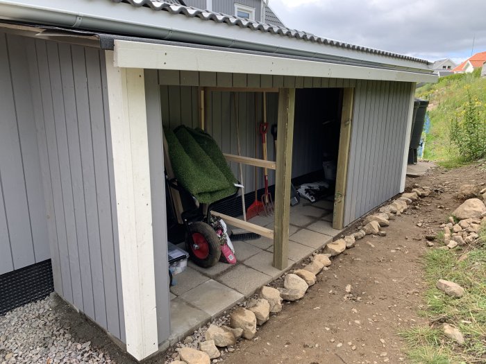 Nästan färdigställd bod utan dörrar och skyddsplåt, med redskap och materiel inuti.