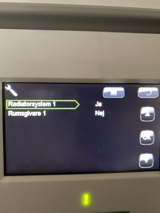 Inställningsmeny på display med alternativen "Radiatorsystem 1 Ja" och "Rumsgivare 1 Nej" samt navigeringsikoner.