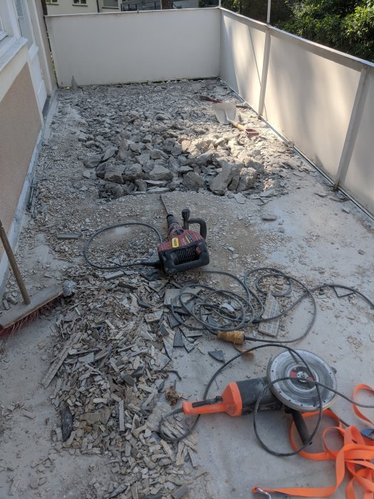 Balkong under renovering med uppbruten betong och verktyg som bilhammare och spikborste.