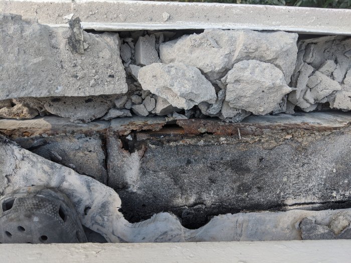 Närbild på en balkongrenovering som visar bortbilad betong, asfaltlager och exponerat träbjälklag.