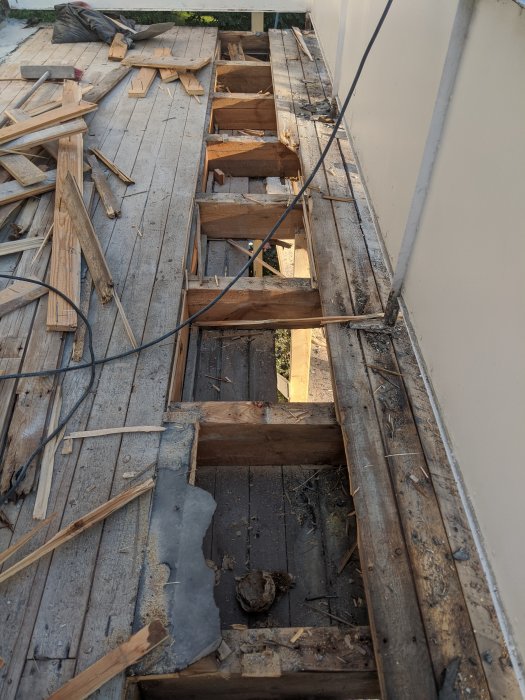 Renoveringsarbete på balkong med borttagen råspont och synliga bjälkar samt verktyg och träavfall.