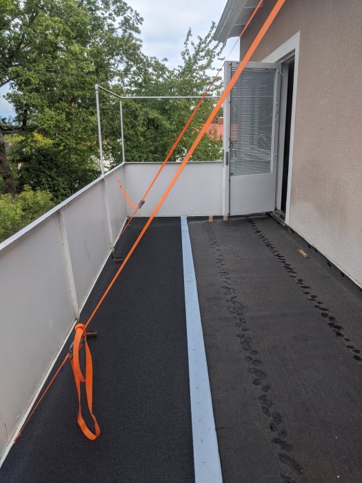 Renoverad balkong med ny takpapp och stödda räcken med spännband under konstruktion.
