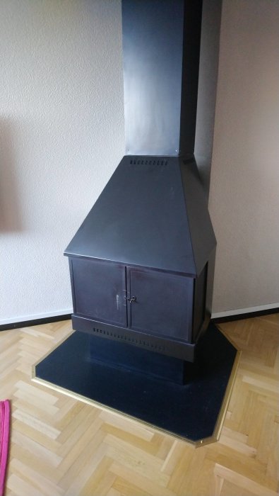 Svart braskamin med skorsten inomhus på parkettgolv till salu i Skurup.