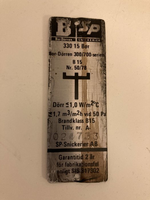 Försliten etikett med teknisk information för en dörr från SP Snickerier, inklusive prestandavärden och serienummer.