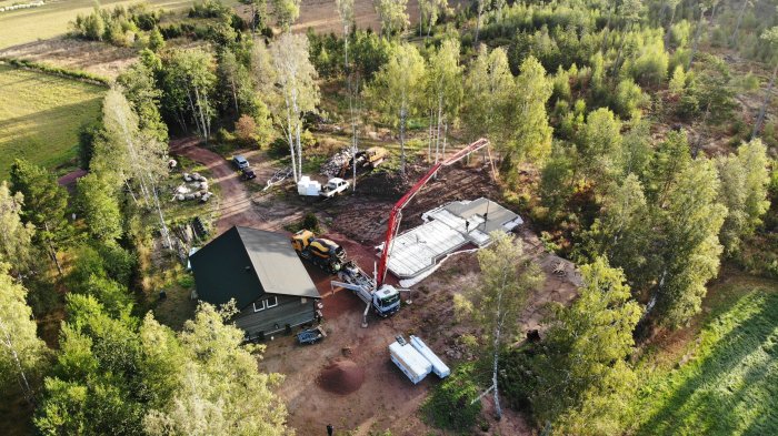 Drönarvy av byggplats med pågående gjutning av betongplatta, byggmaskiner och grön omgivning.