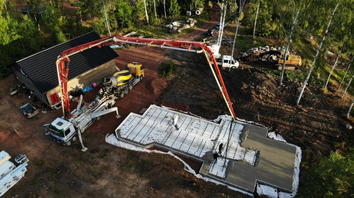 Drönarbild av gjutning av grundplatta med betongpump och arbetare i soligt väder.