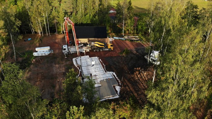 Drönarbild på en nyligen gjuten betongplatta på byggplats med cementblandare och soligt landskap.