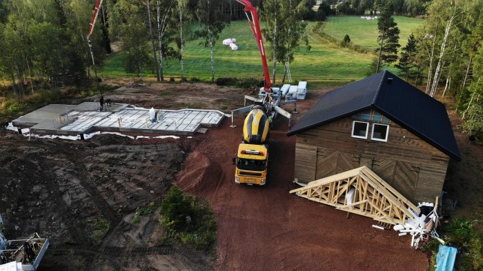 Drönarvy över ett betonggjutningsprojekt med lastbil och byggmaterial bredvid ett hus.