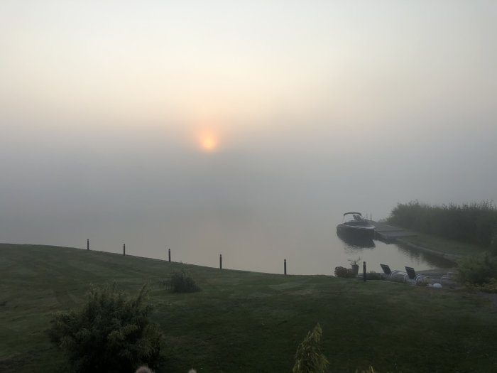 Dimmig morgonvy över stilla vatten med en båt vid en brygga och en sol som knappt syns.