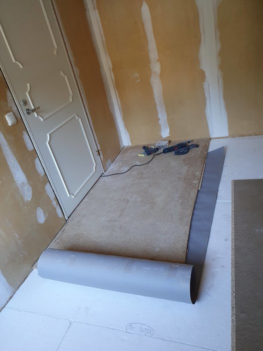 Ett upplyft golvsegment med en rulle papp placerad under i ett pågående renoveringsrum.