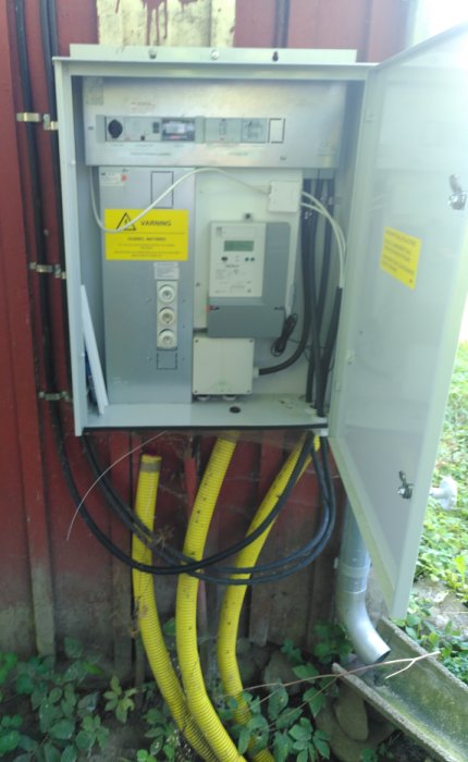 Elektriskt mätarskåp öppet med kablar och tre gula tomrör för anslutning till byggnader.