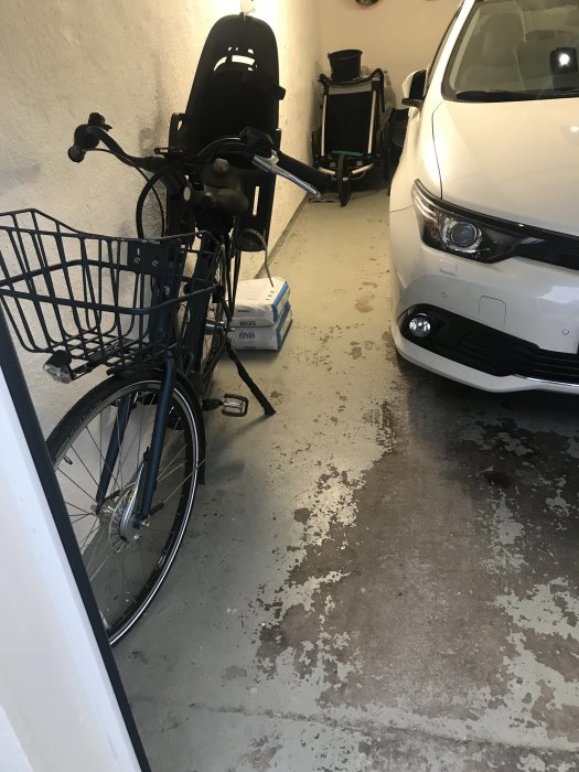 Garage i källare med betonggolv, bil, cykel och verktyg, fläckar och slitage på golvet.