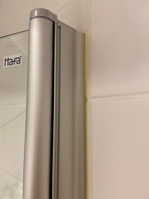 Duschvägg med dåligt applicerad gulaktig fog längs kanten och märken på kaklet.
