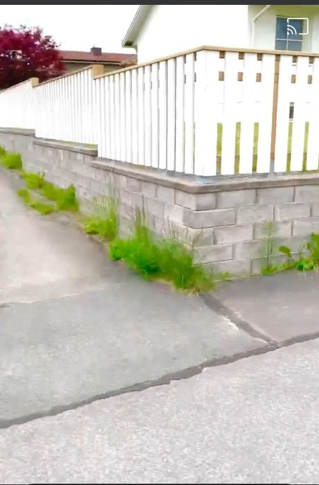 Staket byggt ovanpå en mur längs en gata, högre från gatans synvinkel än inne på tomten.