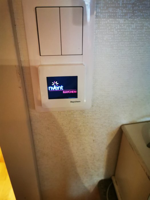 Elektrisk kopplingsdosabox monterad på vägg under strömbrytare med företagslogotyp "nVent RAYCHEM".