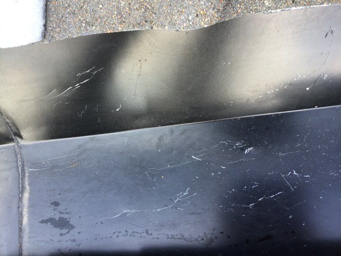 Närbild av svartmålad plåtyta med repor och rispor samt tecken på början till rost.