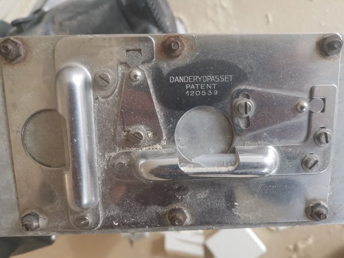 Skadad detalj av Danderydpasset med patentnummer, visar en knust "vatermål" och dammiga metalldelar.