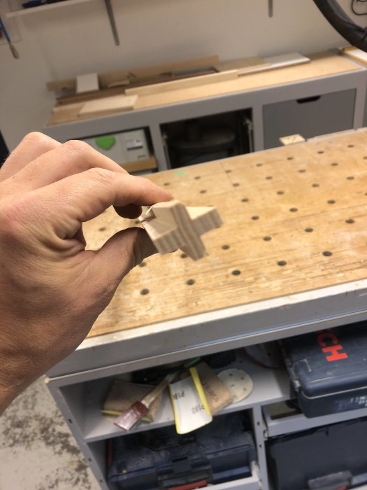 Hand håller ett trästycke ovanför ett fräsbord i en verkstad.