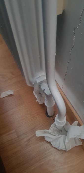 Radiator med synligt packboxproblem vid ventilhus, omsvept med absorberande pappershanddukar på trägolv.