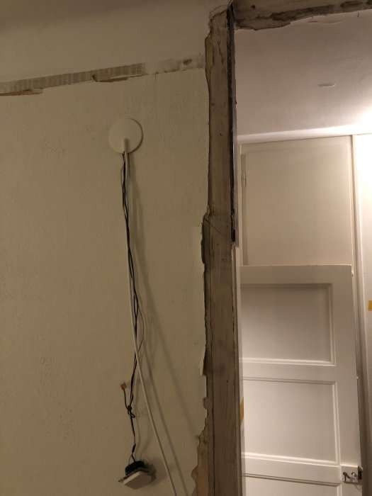 Partially demolished interior wall with exposed edges and hanging wires, awaiting repair and installation of studs to smooth uneven surface.