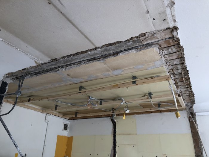 Tak och väggsektion där lättbetongväggar rivits, med exponerade kanaler, kablar och träspikar.