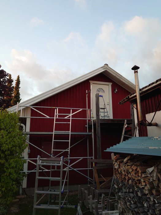 Rödlackerat hus med ställning och stege för målning av takfot och vindskivor.