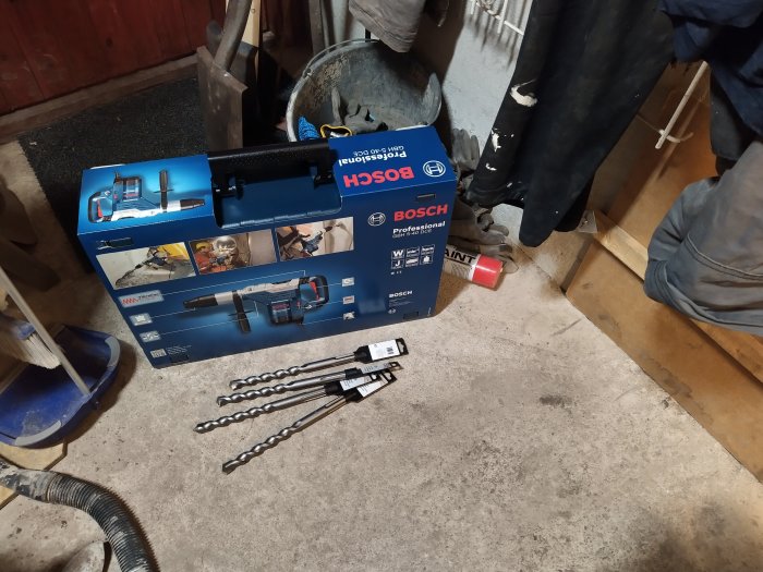 Nytt Bosch borrhammarverktyg och borrset ligger på ett betonggolv vid verktyg och arbetsskor.