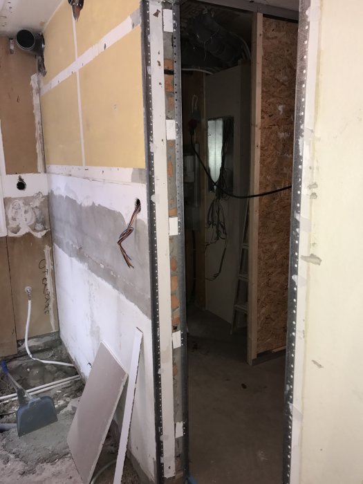 Open doorway in a renovation project with metal corner beads installed, exposed wires, drywall sections, and construction tools visible on the floor.